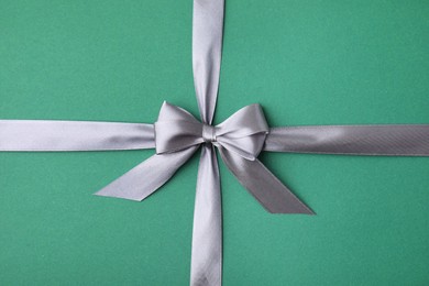 Grey satin ribbon with bow on green background, top view