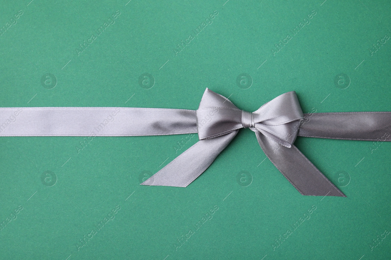 Photo of Grey satin ribbon with bow on green background, top view