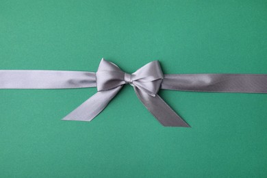 Photo of Grey satin ribbon with bow on green background, top view