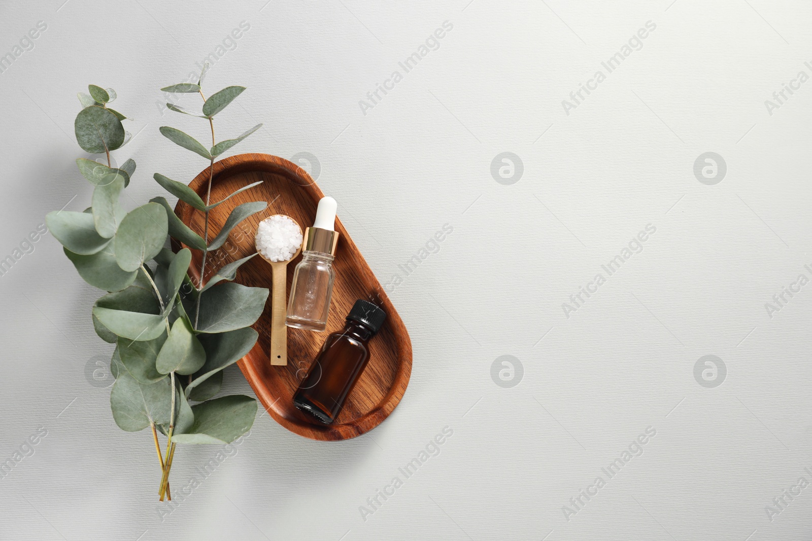 Photo of Aromatherapy products. Bottles of essential oil, sea salt and eucalyptus branches on grey background, flat lay. Space for text