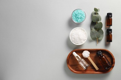 Aromatherapy products. Bottles of essential oil, sea salt and eucalyptus branch on grey background, flat lay. Space for text