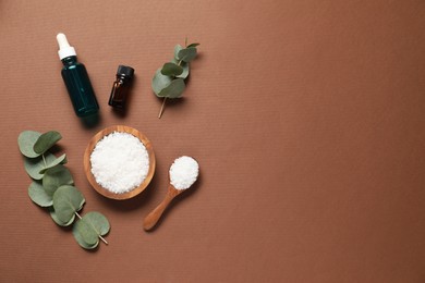 Photo of Aromatherapy products. Bottles of essential oil, sea salt and eucalyptus branches on brown background, flat lay. Space for text