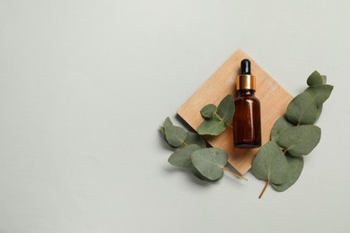 Aromatherapy product. Bottle of essential oil and eucalyptus leaves on grey background, flat lay. Space for text