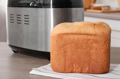 Photo of Breadmaker and fresh homemade bread on wooden table in kitchen, closeup