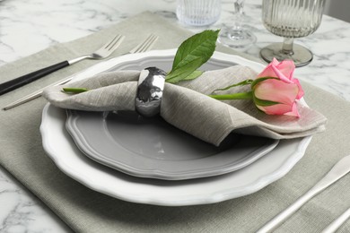 Photo of Stylish setting with cutlery, rose and plates on white marble table