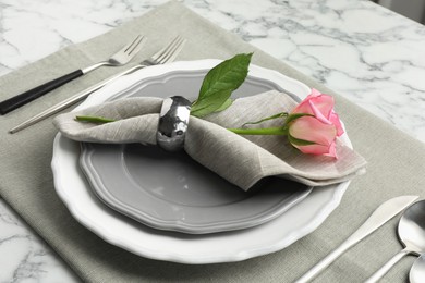 Stylish setting with cutlery, rose and plates on white marble table