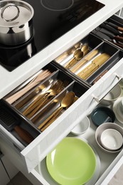 Photo of Ceramic dishware and cutlery in drawers indoors