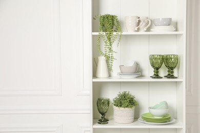 Different clean dishware and houseplants on shelves in cabinet indoors