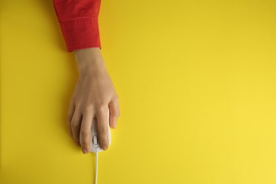 Woman using modern wired computer mouse on yellow background, top view. Space for text