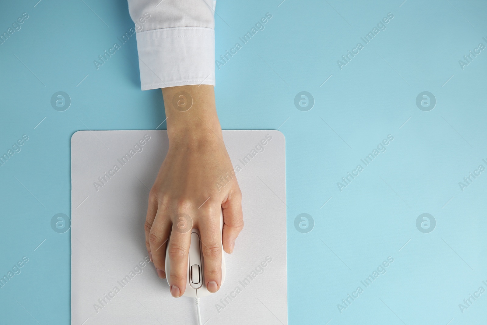 Photo of Woman using modern wired computer mouse on light blue background, top view. Space for text