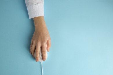 Photo of Woman using modern wired computer mouse on light blue background, top view. Space for text