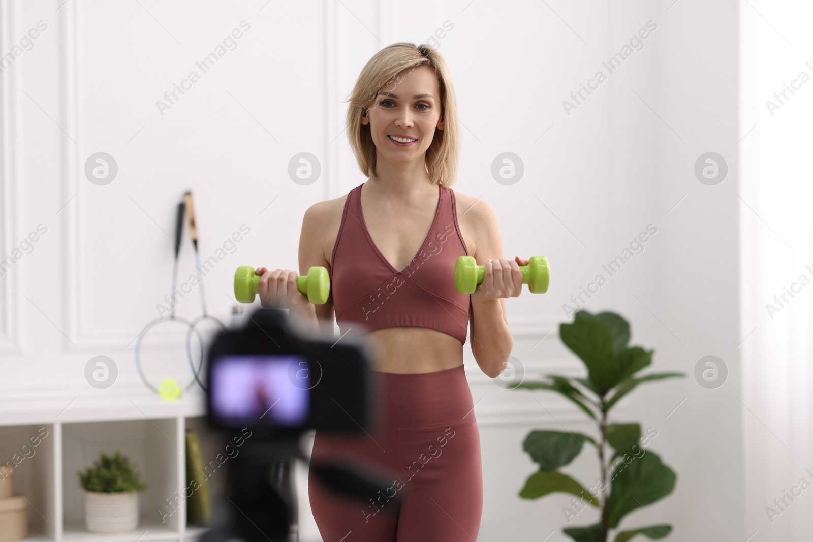 Photo of Smiling sports blogger working out with dumbbells while recording fitness lesson at home