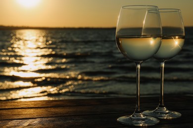 Photo of Two glasses of wine on wooden table near river at sunset. Space for text