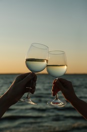 Women clinking glasses of wine near river at sunset, closeup