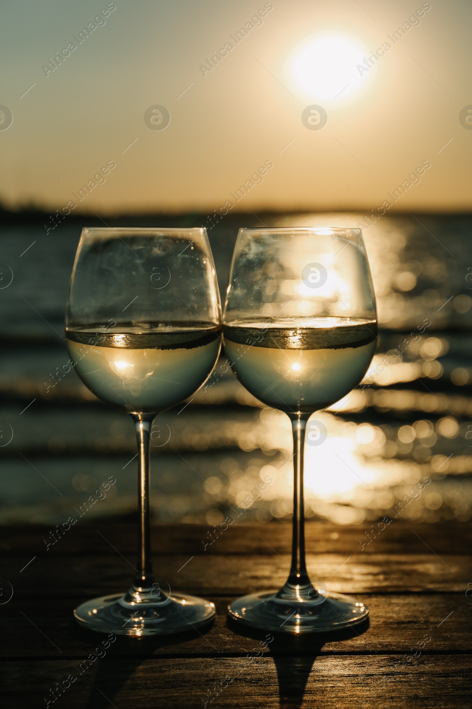 Photo of Two glasses of wine on wooden table near river at sunset