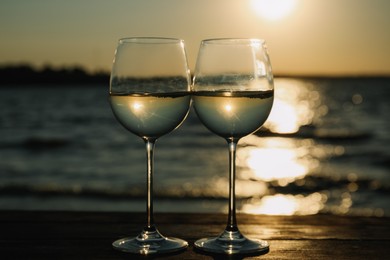 Photo of Two glasses of wine on wooden table near river at sunset