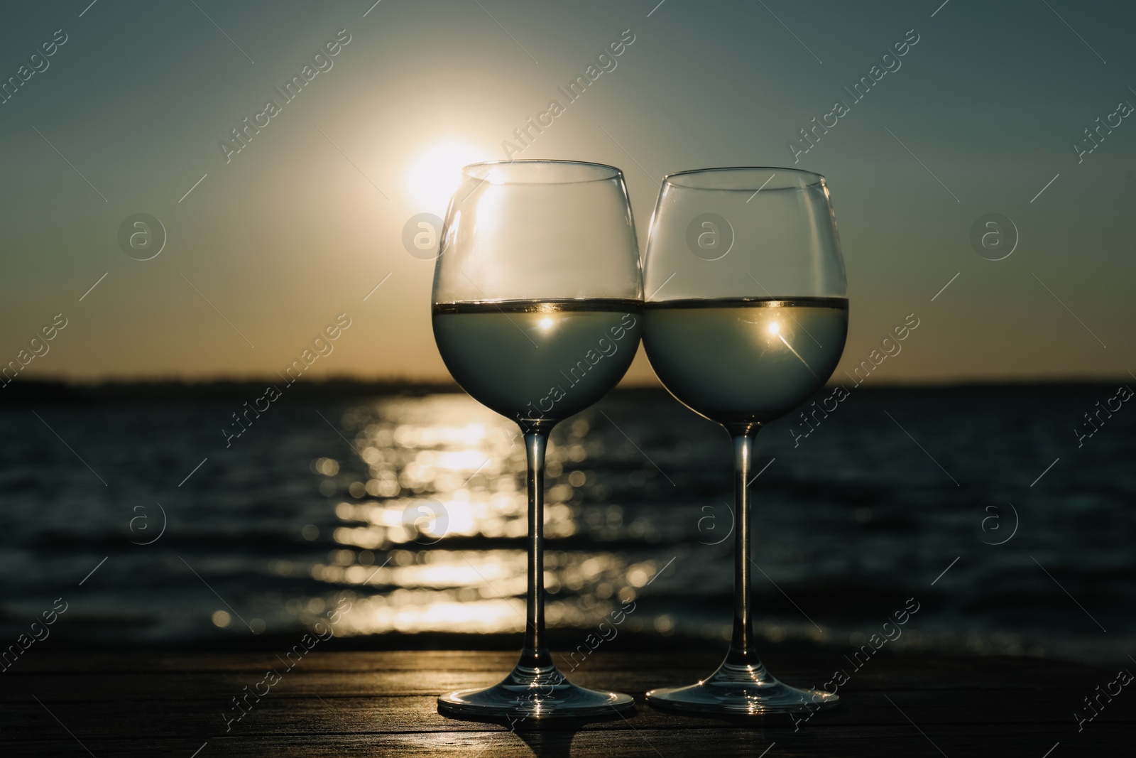 Photo of Two glasses of wine on wooden table near river at sunset