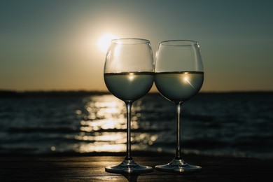 Photo of Two glasses of wine on wooden table near river at sunset