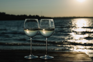 Photo of Two glasses of wine on wooden table near river at sunset. Space for text