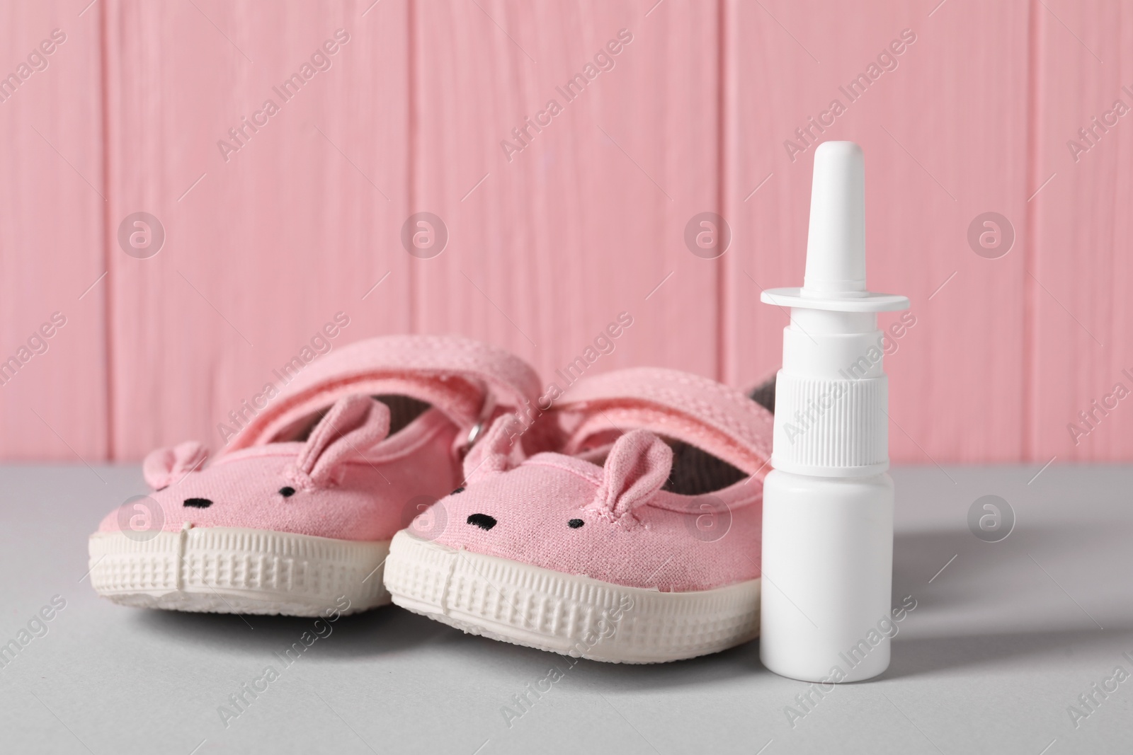 Photo of Cute baby shoes and nasal spray on grey table, closeup