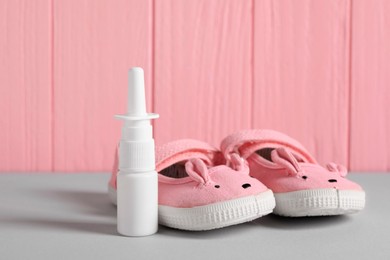 Cute baby shoes and nasal spray on grey table, closeup