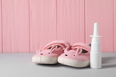 Photo of Cute baby shoes and nasal spray on grey table, closeup