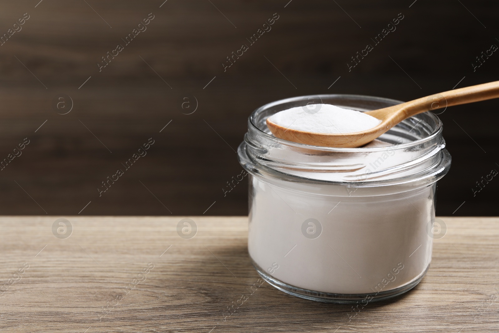 Photo of Baking soda in glass jar on wooden table, space for text