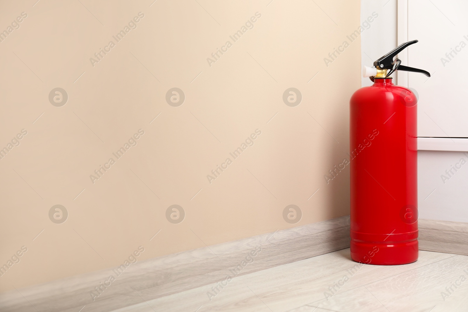 Photo of Fire extinguisher on floor near beige wall indoors, space for text