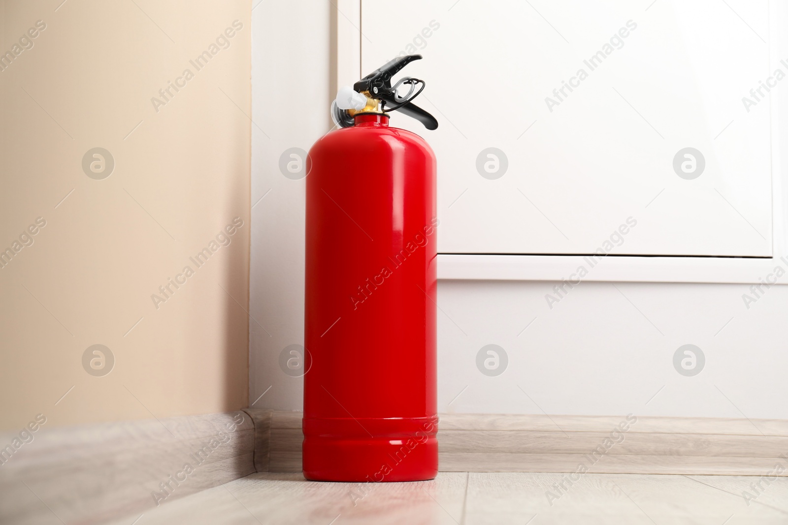 Photo of Fire extinguisher on floor near beige wall indoors