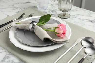 Photo of Stylish setting with cutlery, rose and plates on white marble table