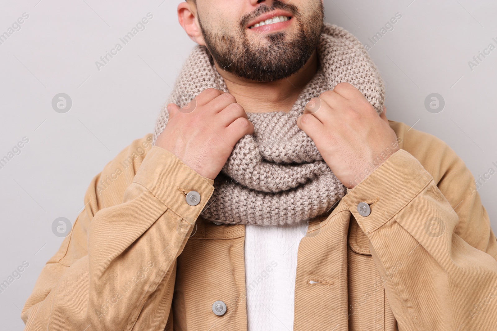 Photo of Smiling man in warm scarf on light grey background, closeup
