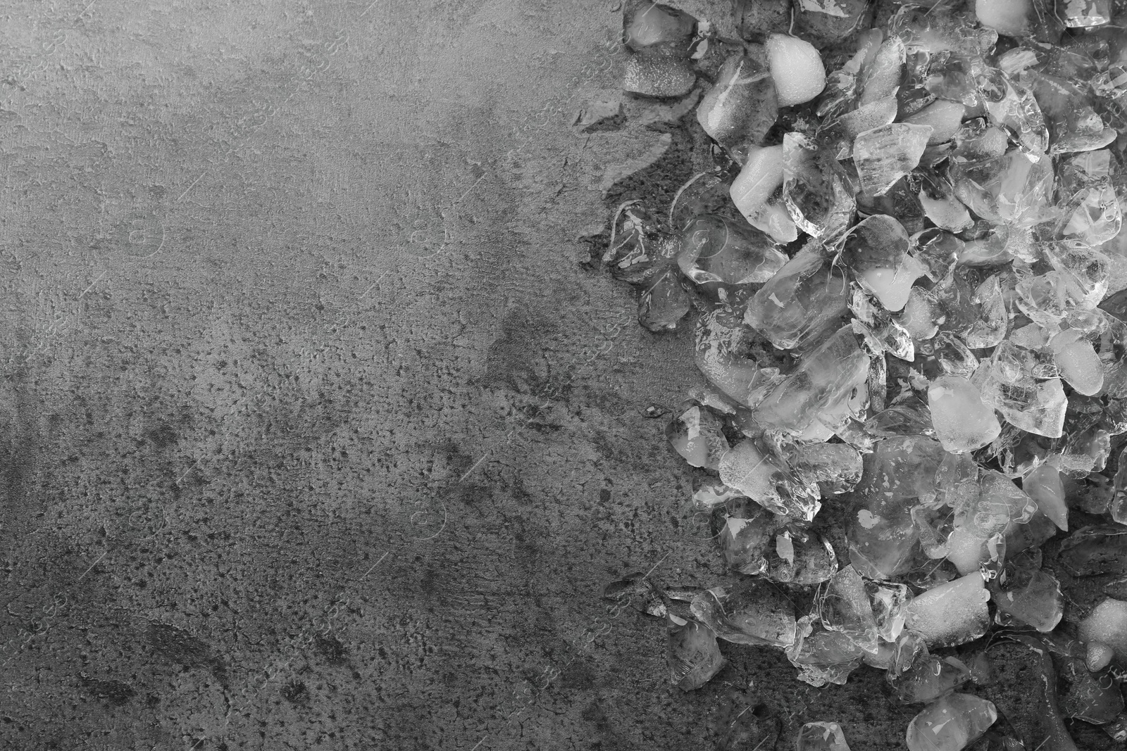 Photo of Pieces of crushed ice on dark textured table, top view. Space for text