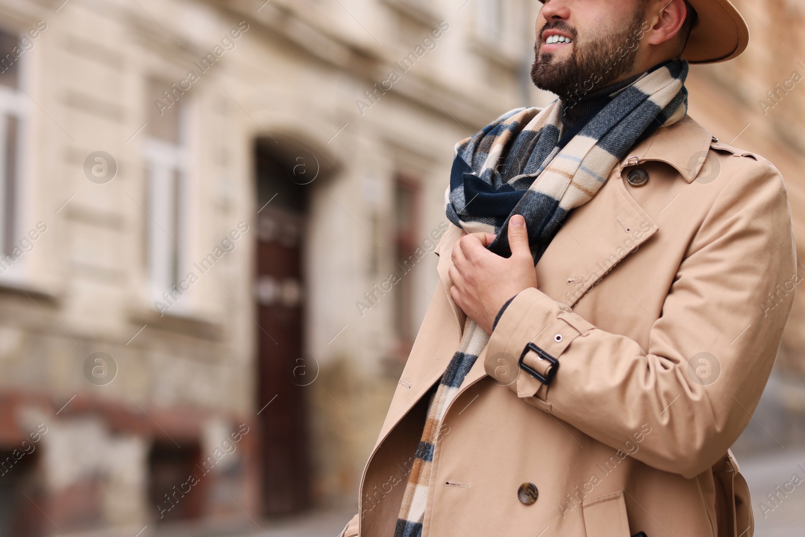 Photo of Smiling man in warm scarf on city street, closeup. Space for text