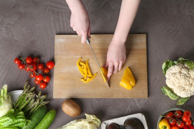 Healthy food. Woman cutting pepper at gray textured table, top view