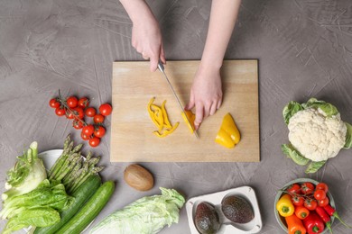 Photo of Healthy food. Woman cutting pepper at gray textured table, top view