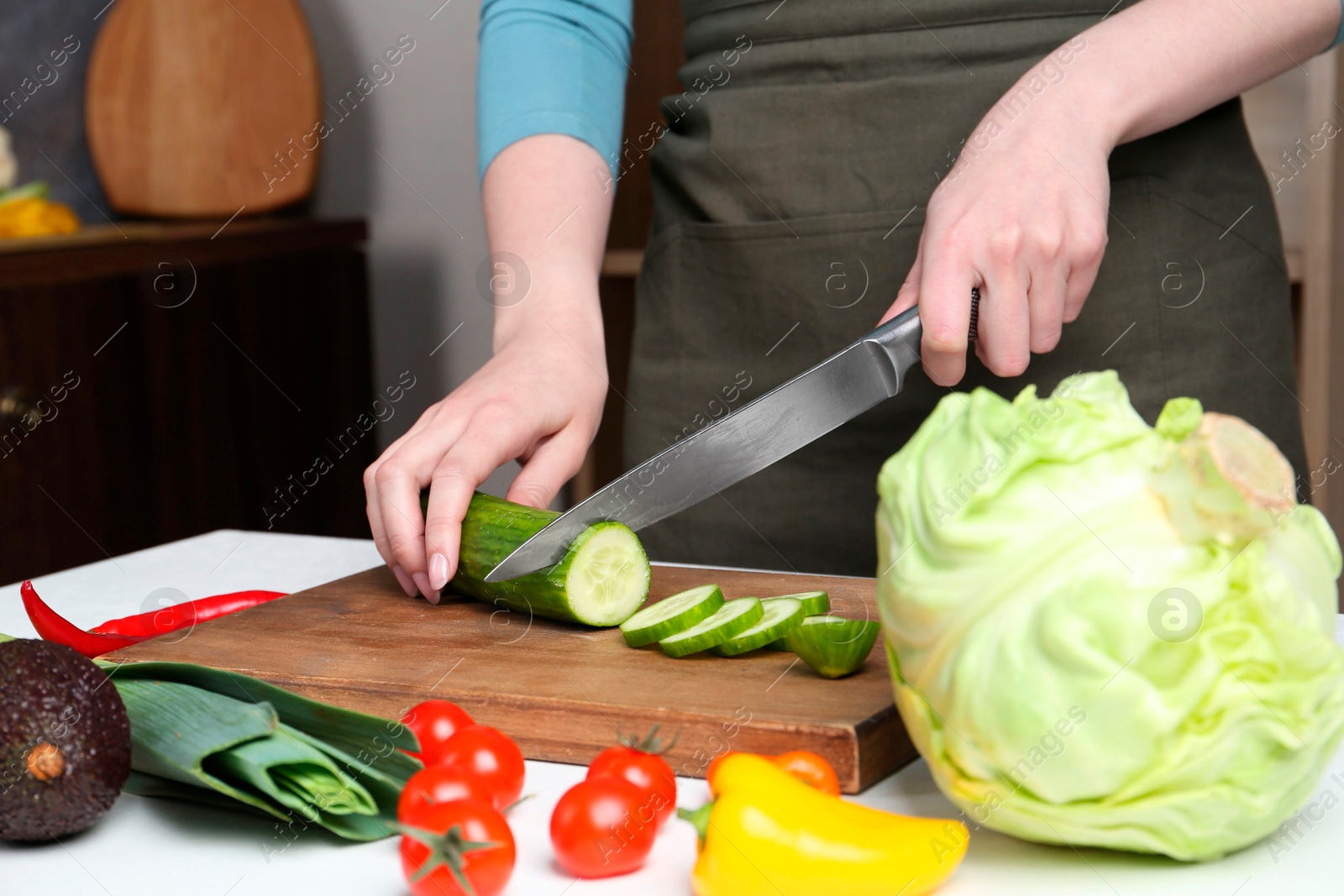 Photo of Healthy food. Woman cutting cucumber at white table, closeup