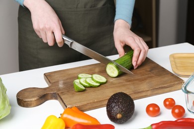 Photo of Healthy food. Woman cutting cucumber at white table, closeup