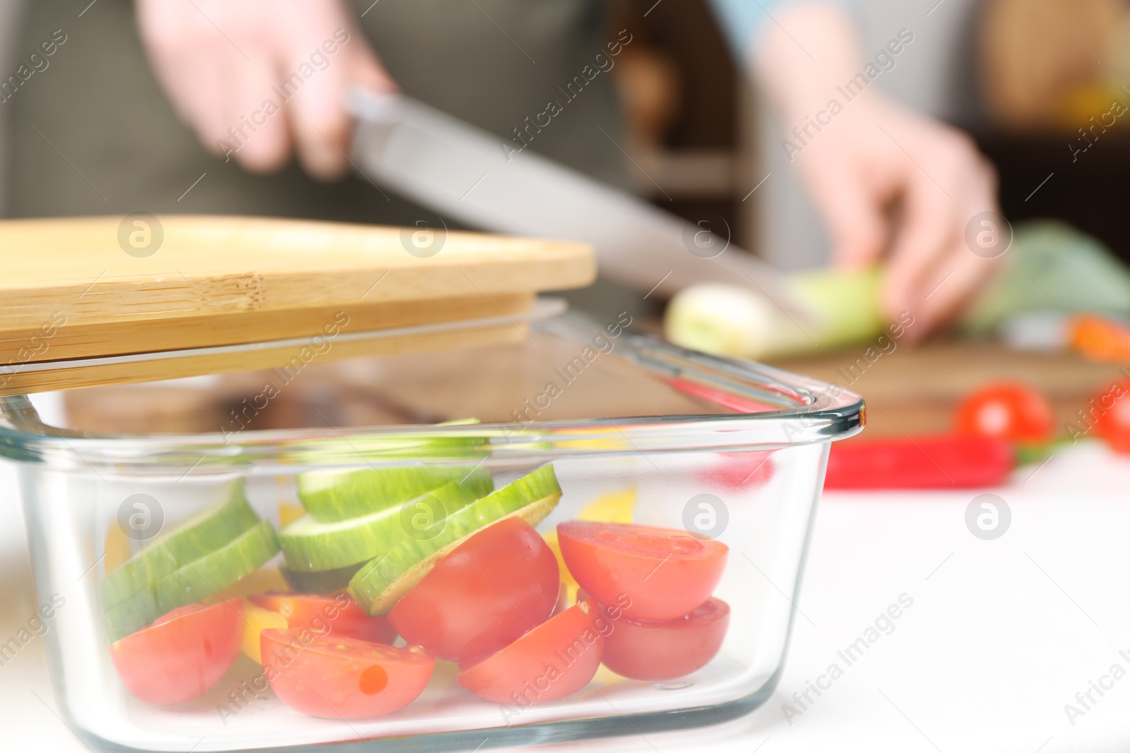 Photo of Healthy food. Woman cutting leek at white table, focus on glass container with sliced vegetables