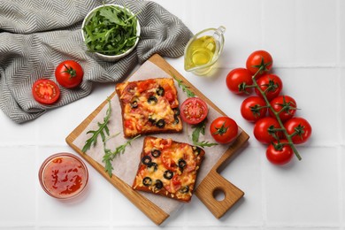 Photo of Tasty pizza toasts and ingredients on white tiled table, flat lay