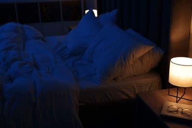 Photo of Nightlight, glasses and book on bedside table near bed indoors