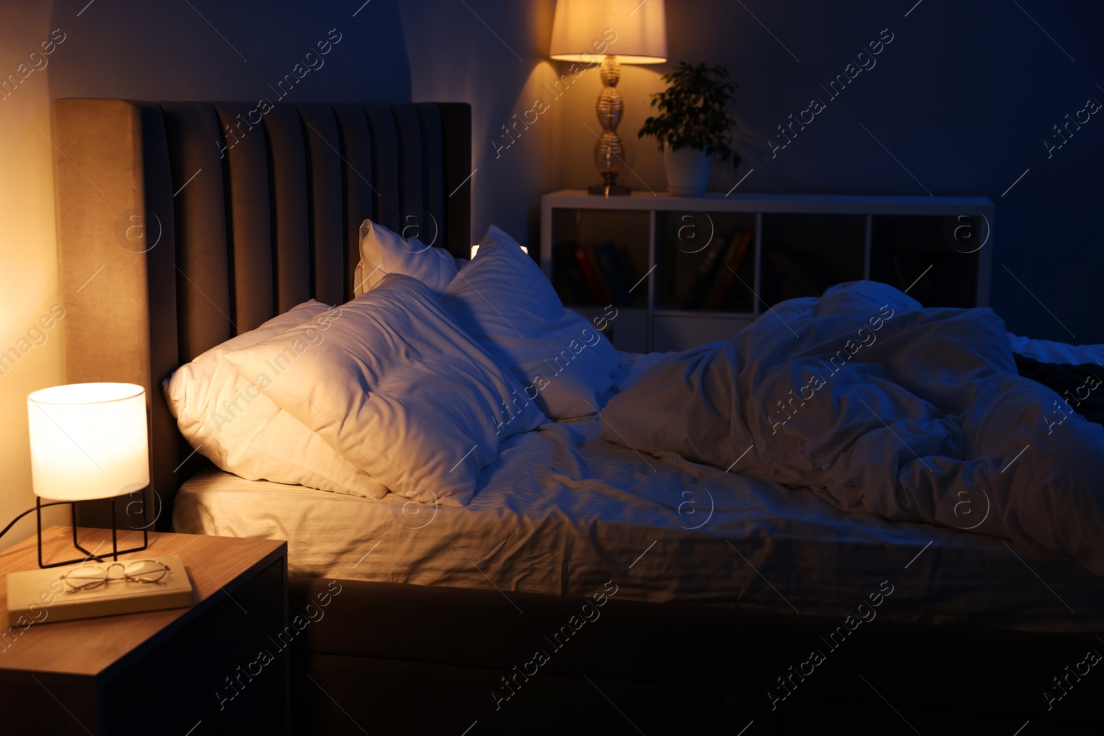 Photo of Nightlight, glasses and book on bedside table near bed indoors