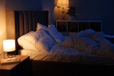 Photo of Nightlight, glasses and book on bedside table near bed indoors