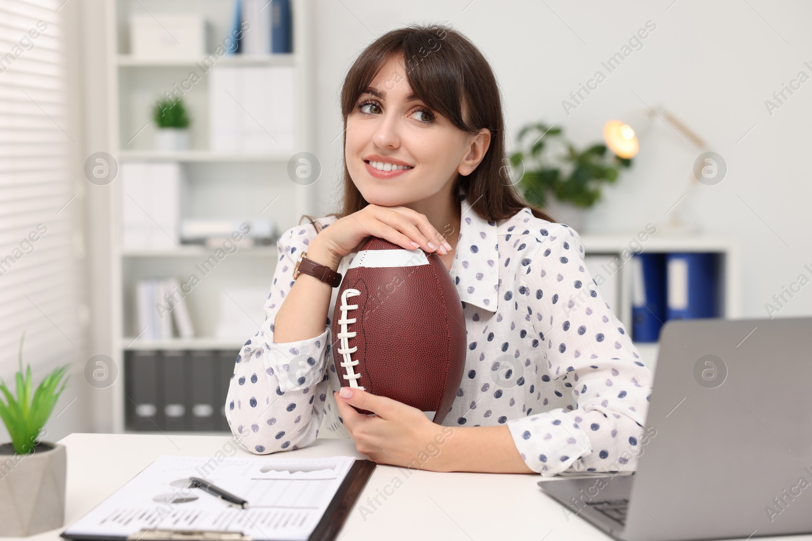 Photo of Smiling employee with american football ball at table in office