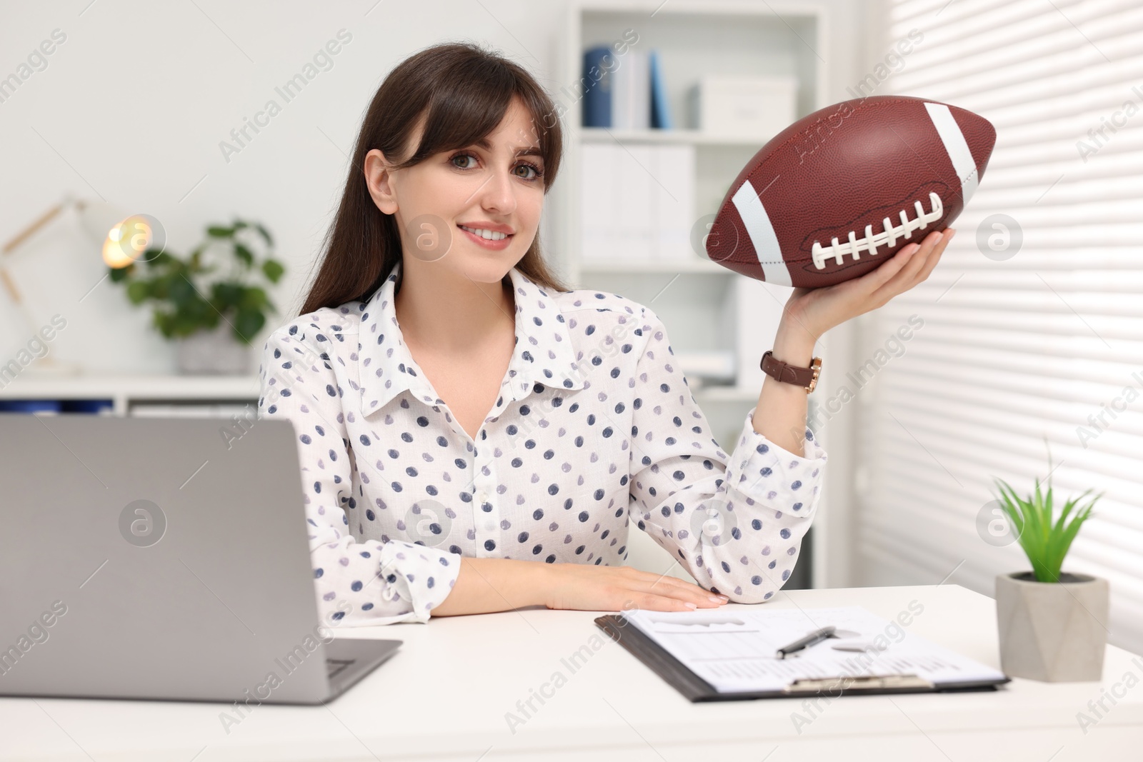 Photo of Smiling employee with american football ball at table in office