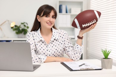 Smiling employee with american football ball at table in office