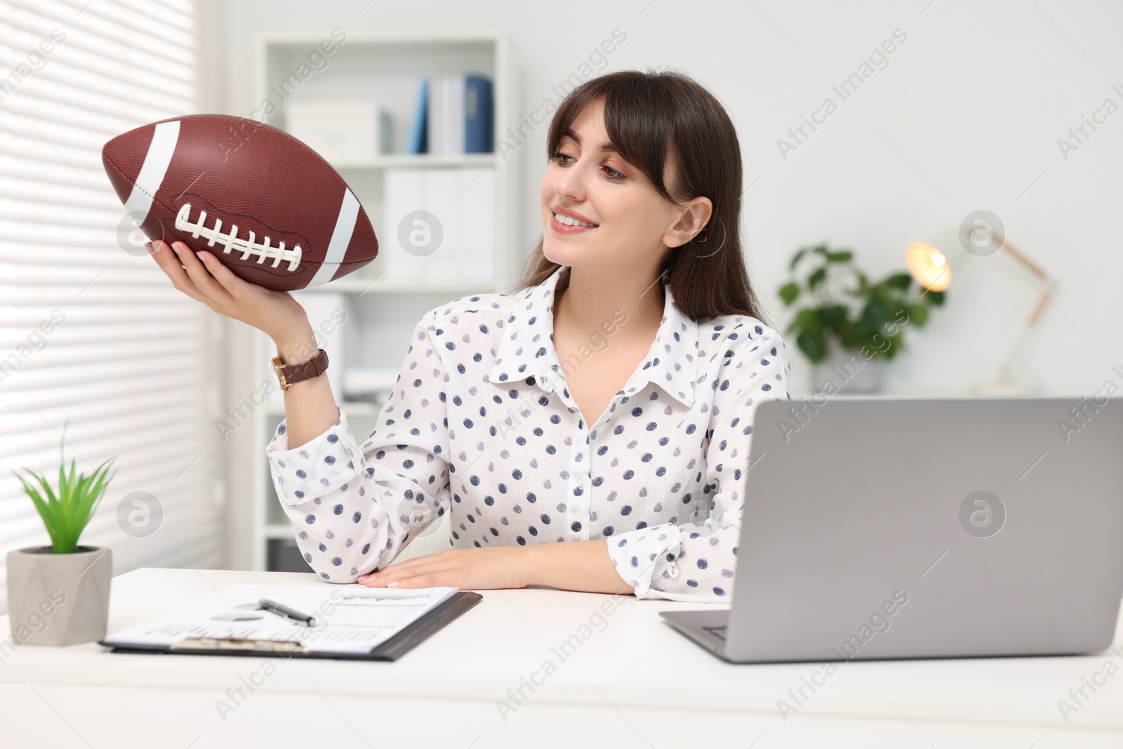 Photo of Smiling employee with american football ball at table in office