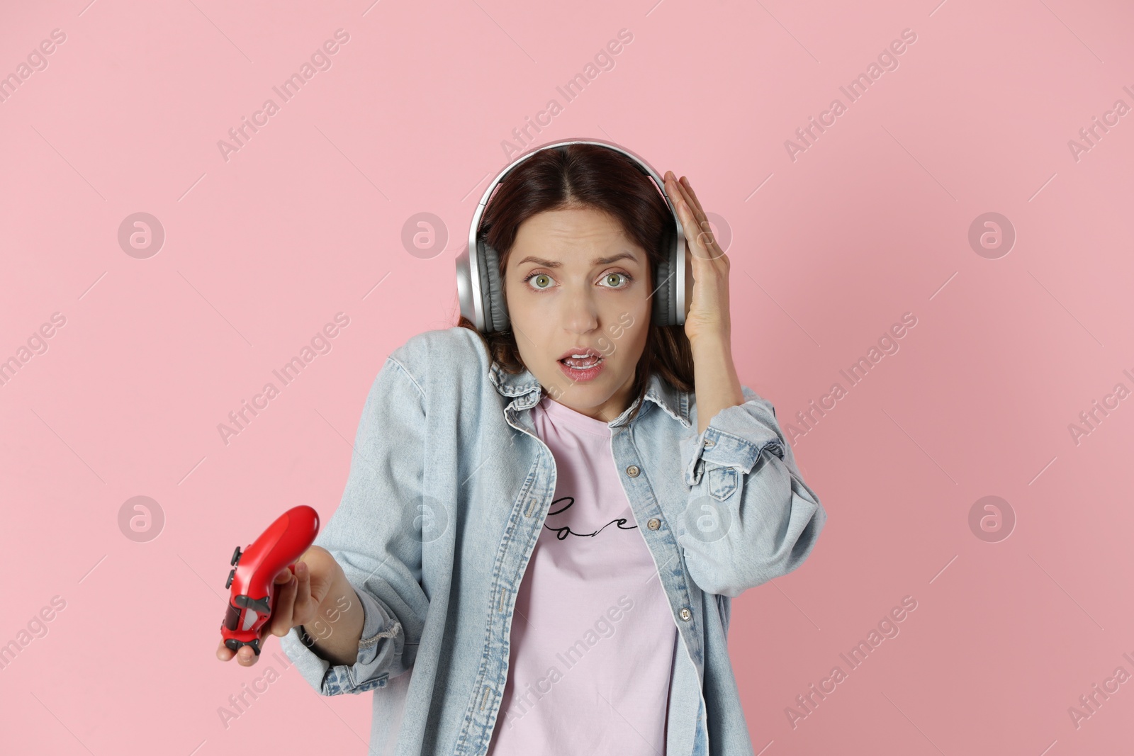 Photo of Emotional woman in headphones with game controller on pink background