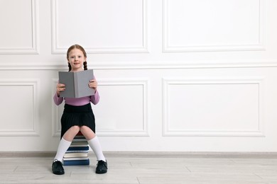Photo of Little girl sitting on stack of books indoors. Space for text