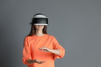 Photo of Smiling woman using virtual reality headset on gray background, space for text