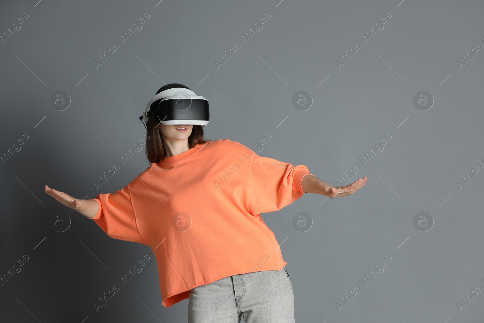 Photo of Woman using virtual reality headset on gray background, space for text